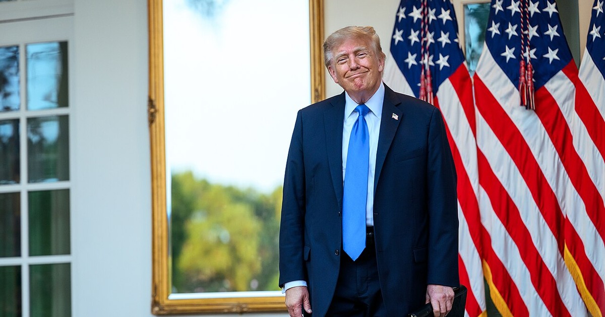 President Donald Trump standing beside American flags at the White House